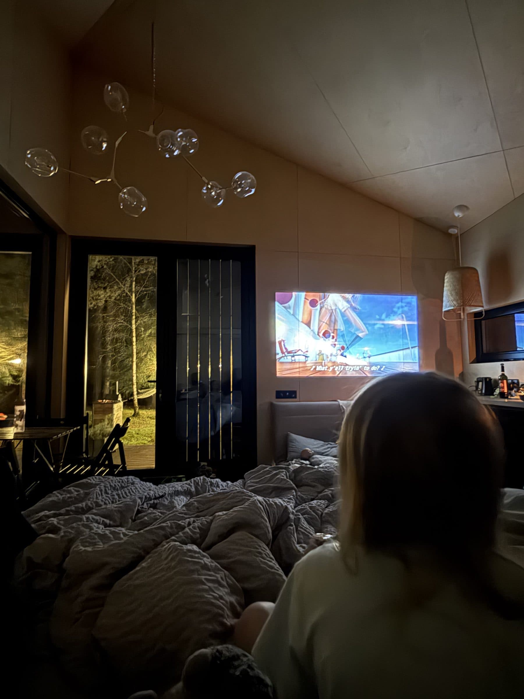 Film projected on the wall above the bed, forest in the door